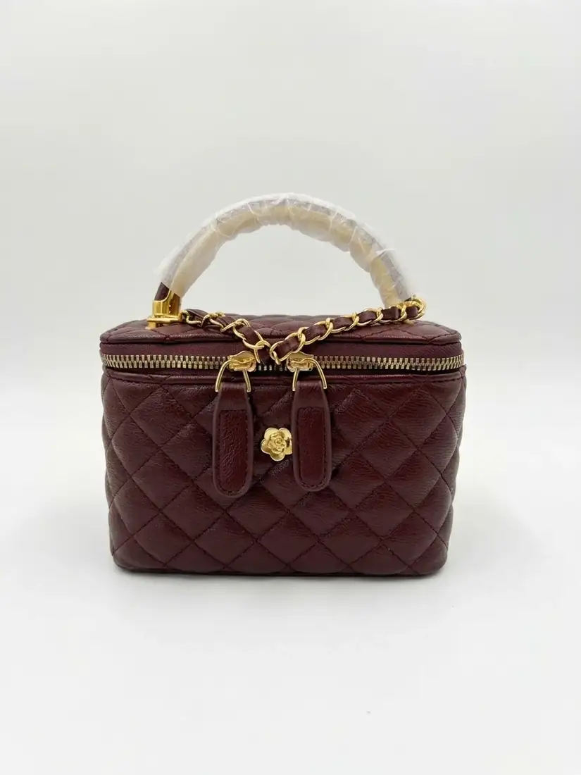Cartera granate con rombos acolchados, asa superior, cremallera y detalles de tono dorado.